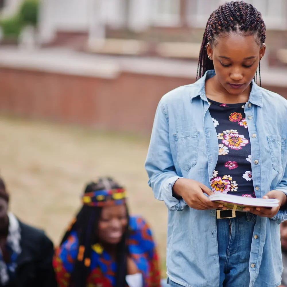 A young woman is engrossed in a book, surrounded by a group of engaged listeners.