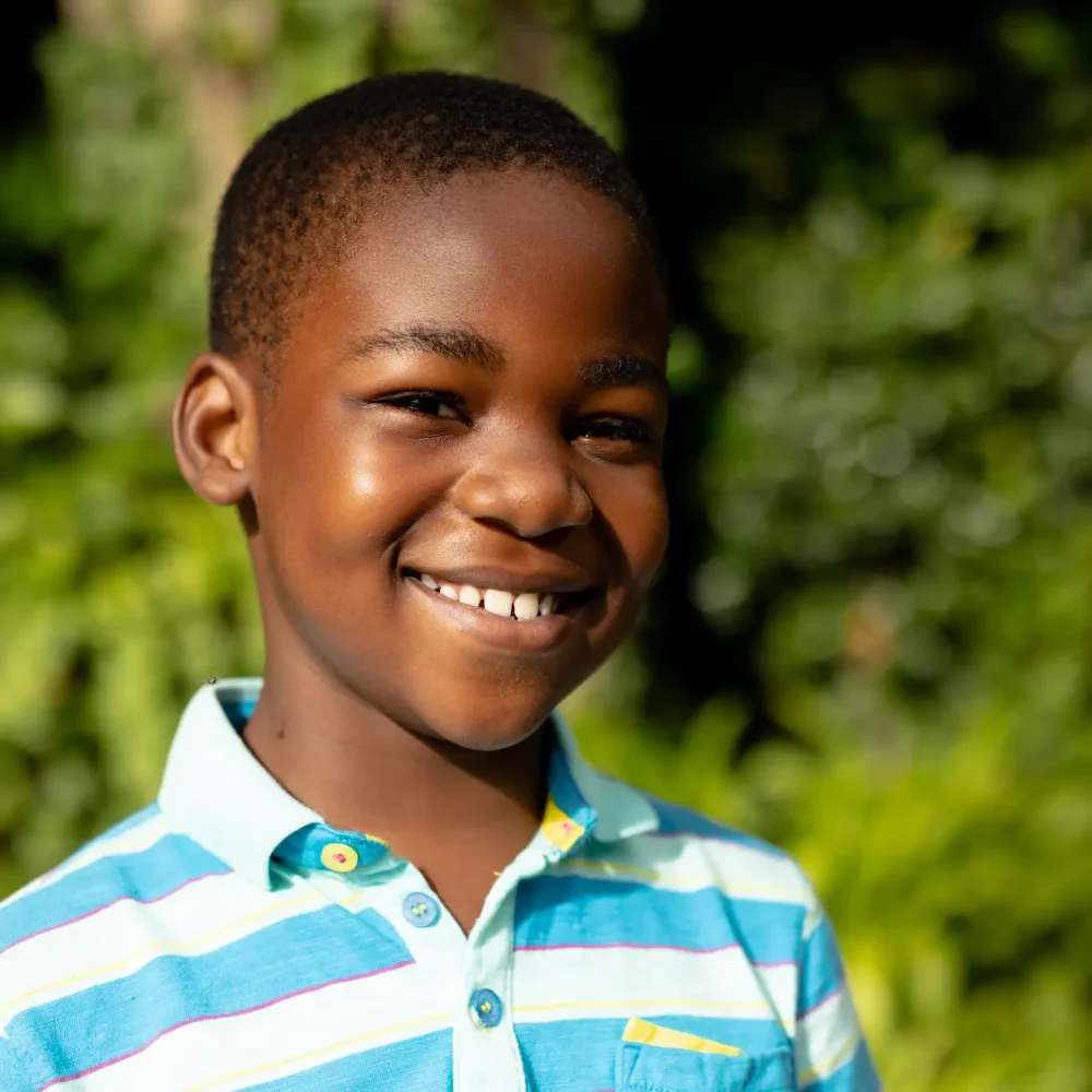 A cheerful young African boy poses for the camera, his smile radiating happiness and warmth.
